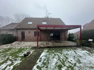 Arrière de maison en briques avec pergola rouge et terrasse en construction, sol enneigé.