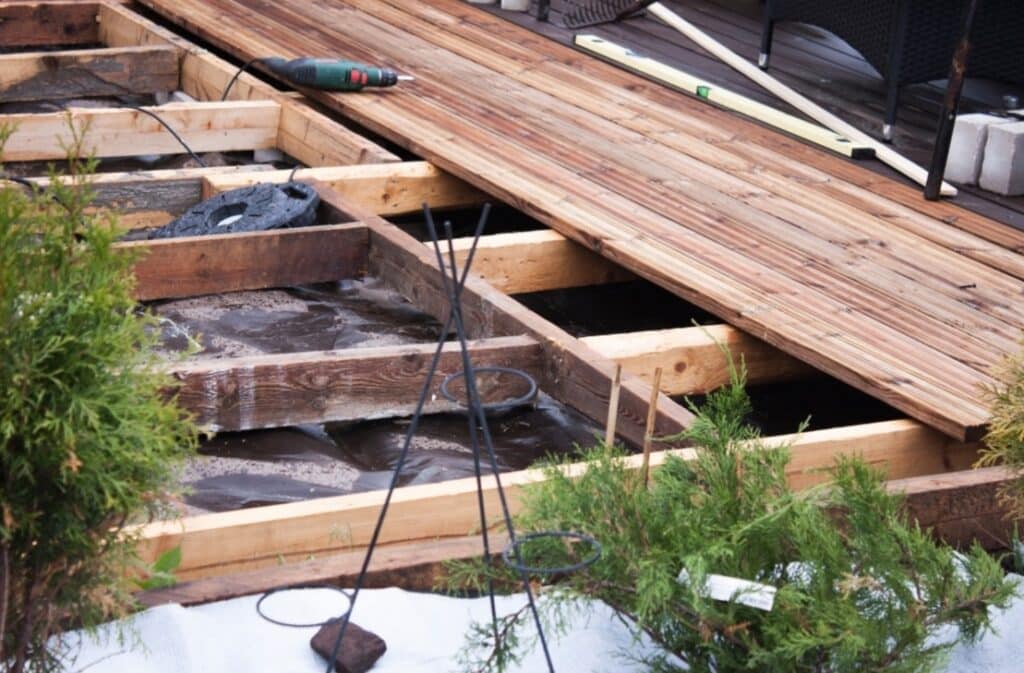 Terrasse Bois en Construction: Structure et Outils Terrasse en bois en construction, lambourdes apparentes sur bâche noire mouillée. Perceuse et niveau outils de chantier.